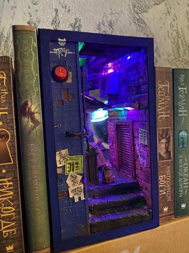 Cyberpunk city cool bookends inspired by the game Stray, featuring neon purple lighting, urban graffiti, and a tiny ginger cat sitting on a ledge.