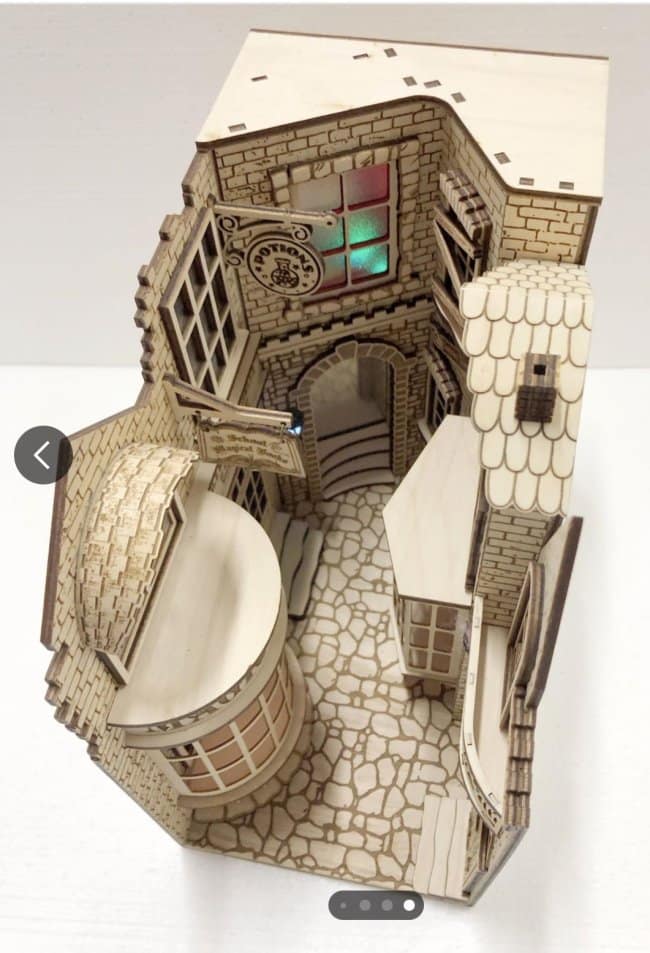 Intricate laser-cut wood wizard alley cool bookends showcasing the unpainted assembly of a miniature magical street with hanging signs and arched doorways.