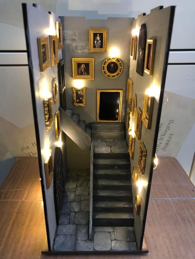 Grand castle hall cool bookends featuring a miniature gray stone staircase flanked by walls covered in tiny gold-framed paintings under warm spotlighting.