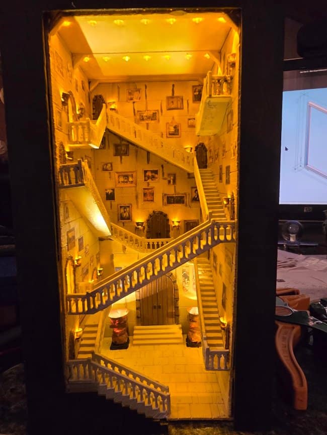 Enchanted school grand staircase cool bookends with finished stonework, multiple levels of miniature stairs, and a golden glow illuminating a wall of portraits.