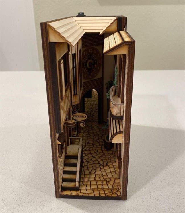 Rustic laser-cut wood alley cool bookends showing a miniature pizzeria with a balcony and a distant clock tower viewed through a narrow street corner.
