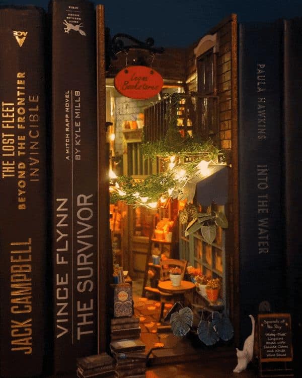 Nighttime bookstore street cool bookends featuring fairy lights woven through ivy, a red bookstore sign, and tiny stacks of books resting on the cobblestones.