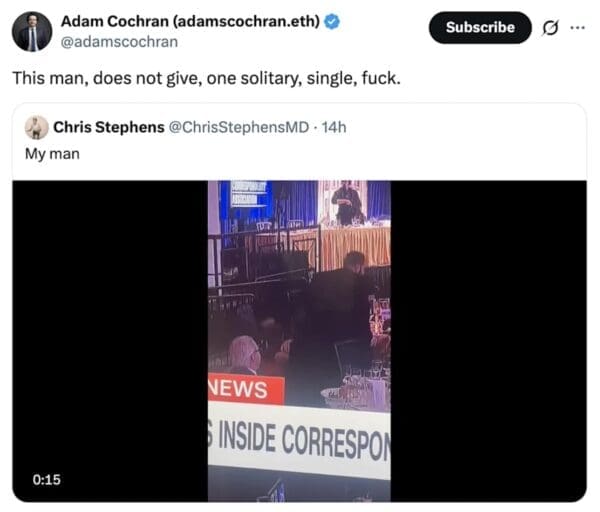 A viral correspondents dinner meme captured in a low-res news still. While a security guard moves in the background, a guest sits perfectly still, focused entirely on his plate. The tweet from Adam Cochran summarizes the man’s vibe: "This man, does not give, one solitary, single, f*ck."