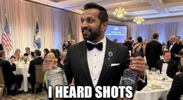 correspondents dinner meme featuring Kash Patel in a formal black tuxedo and bowtie. He is smiling widely while holding up two large bottles of alcohol—one Patron tequila and one Jack Daniel's whiskey. The bold text at the bottom reads: "I HEARD SHOTS."