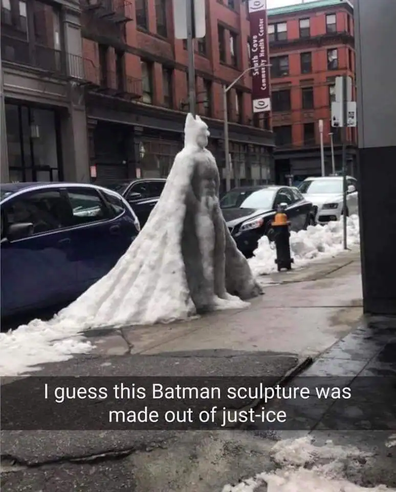 visual dad joke showing an impressively detailed Batman sculpture carved entirely out of a pile of snow on a city sidewalk. The Snapchat-style caption reads: "I guess this Batman sculpture was made out of just-ice."