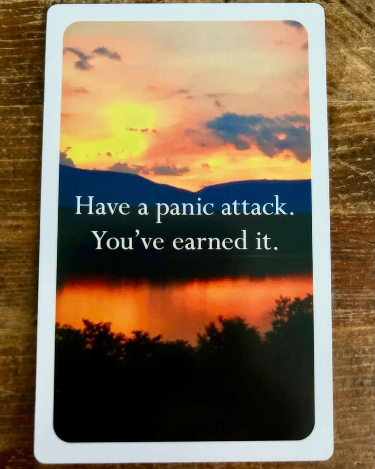 Demotivational quote card on sunset lake encouraging readers to have the panic attack they've fully earned.