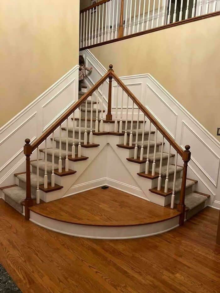 A confusing architectural design fail where a central wooden staircase platform splits into two identical sets of stairs leading to the same upper hallway, serving as a redundant and space-consuming example of questionable home decor.