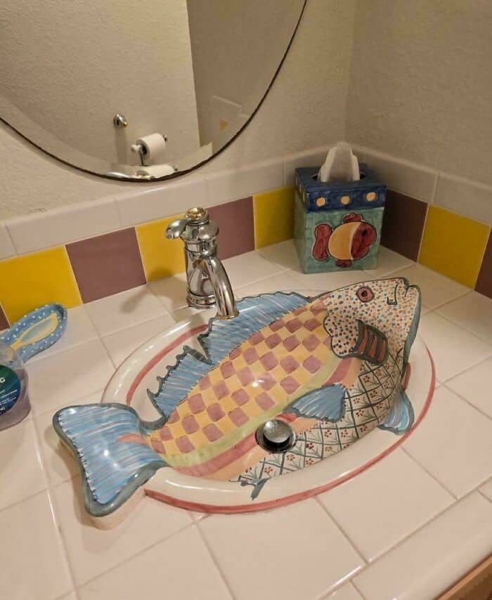 A themed bathroom featuring questionable home decor in the form of a ceramic sink shaped and painted like a large, colorful, spotted fish, complete with a matching folk-art fish tissue box cover.