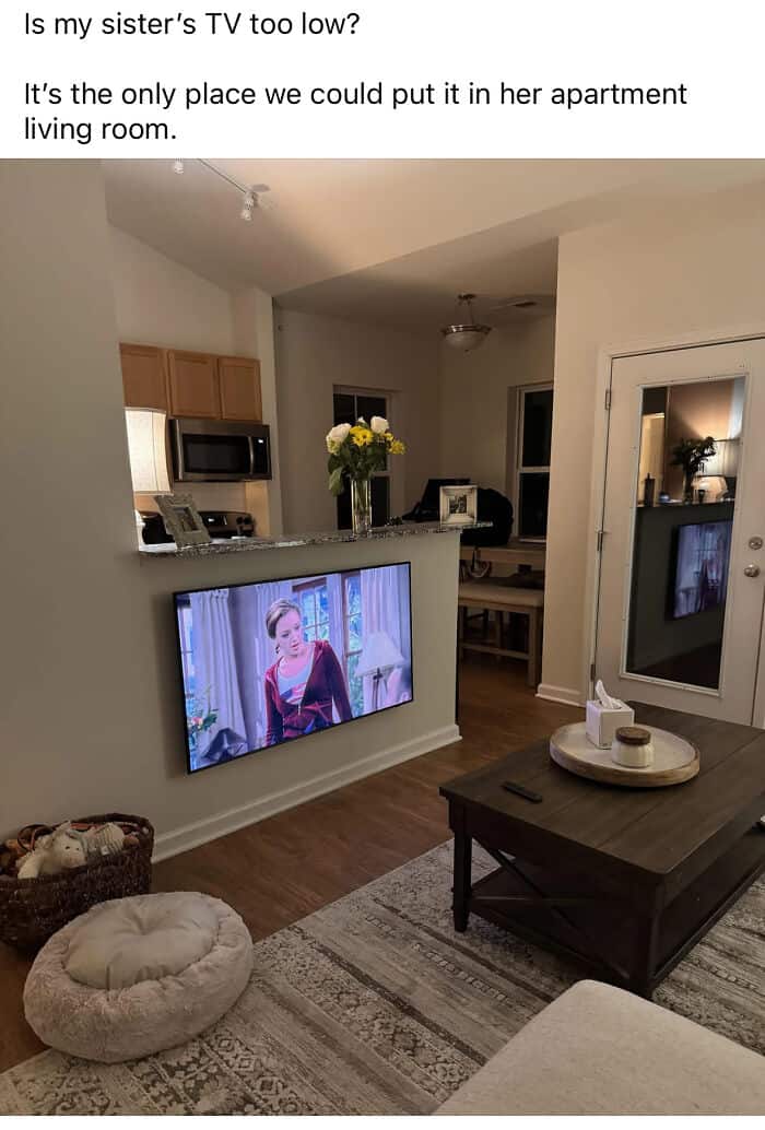 A literal "TV too low" design fail where a flat-screen television is mounted just inches above the floor on a pony wall. This questionable home decor choice forces viewers to look downward while sitting on the sofa.