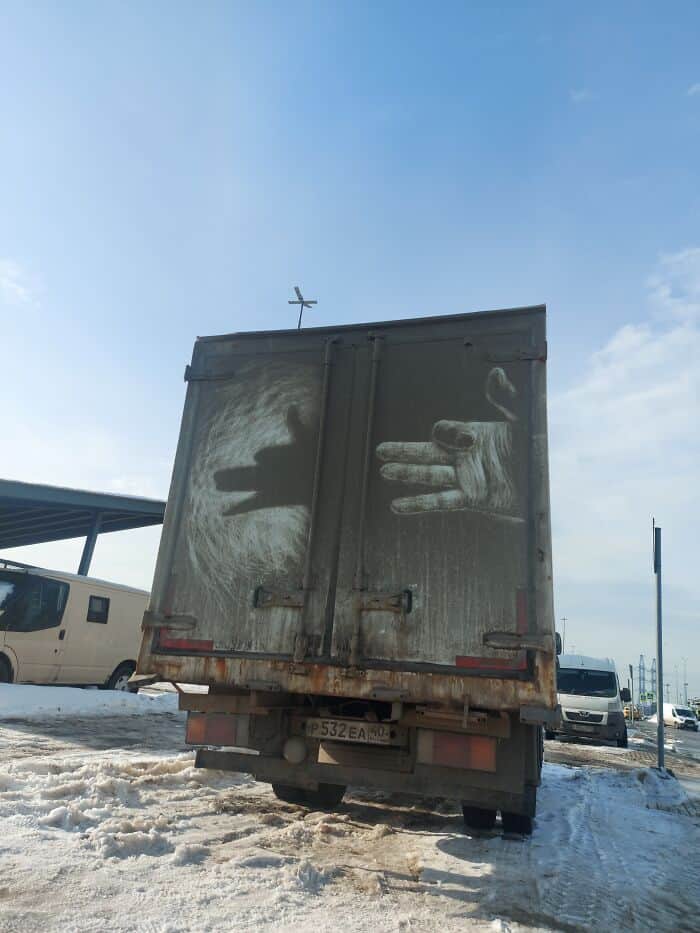 Hand shadow puppet of a dog etched into thick dirt on the back of a truck.