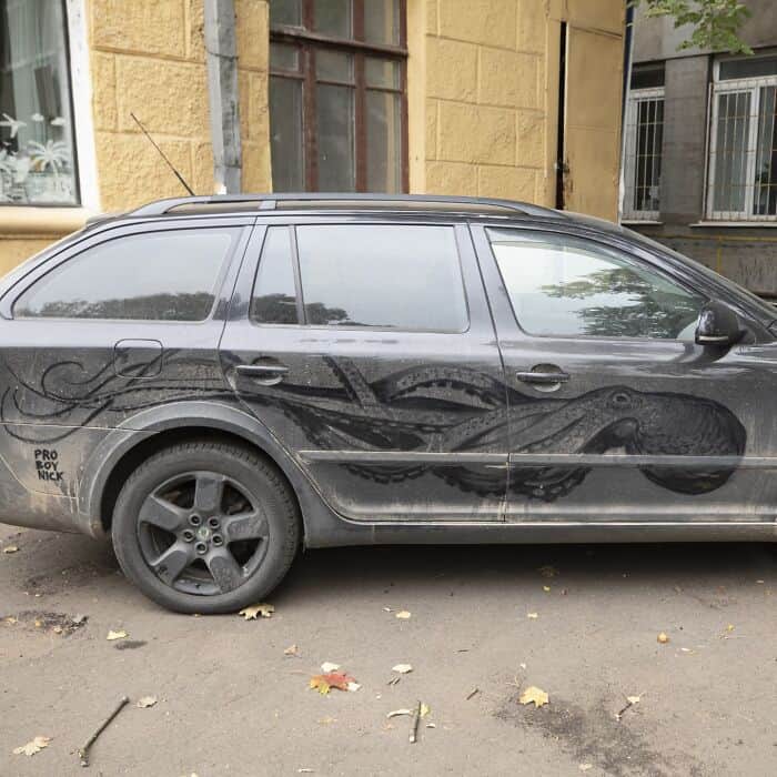 Large octopus with detailed tentacles drawn into the dirt on the side of a car.