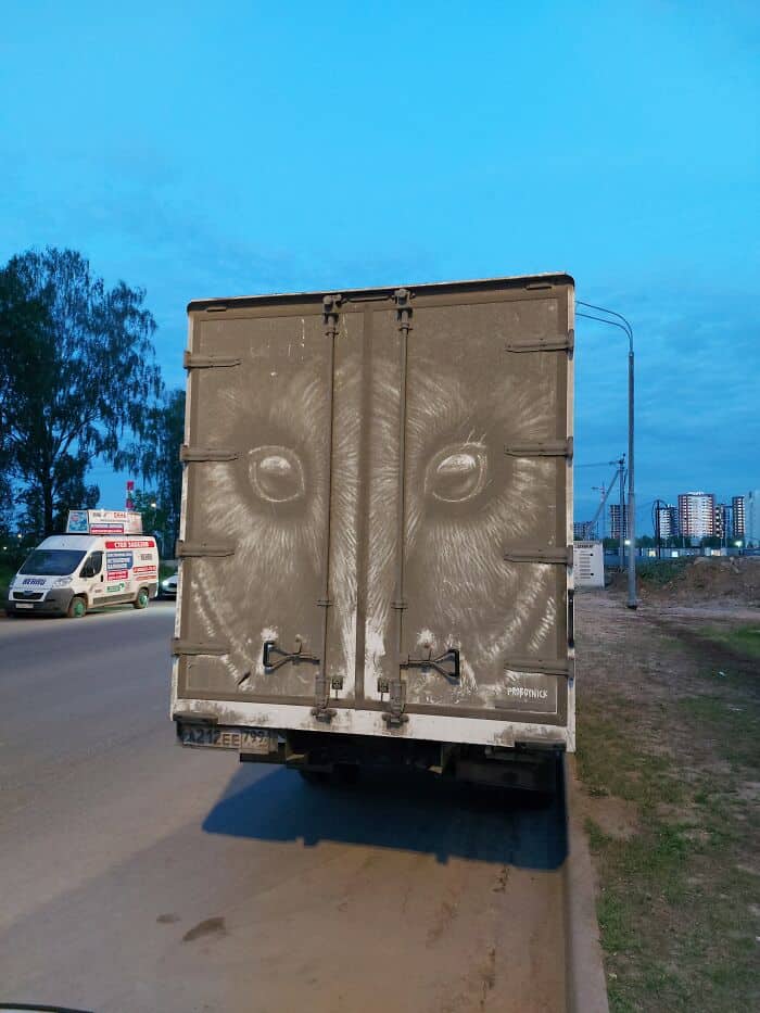 Two large, intense animal eyes etched into the back of a dirty cargo truck.