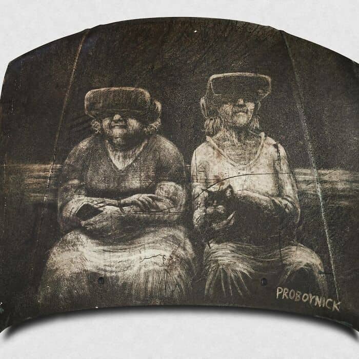 Dirt art on a car hood depicting two elderly women wearing virtual reality headsets.