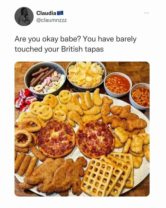 self-deprecating funny british tweet by user Claudia featuring a massive "British tapas" platter. The board is piled high with a beige feast of childhood staples: turkey dinosaurs, smiley faces, potato waffles, chicken nuggets, mini pepperoni pizzas, and side bowls of baked beans and spaghetti hoops.