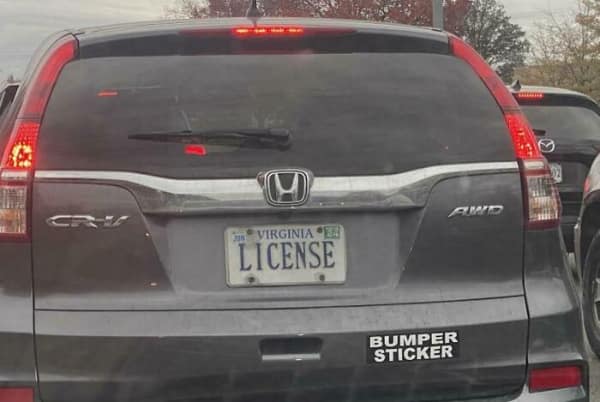 A small, square-ish [funny bumper sticker] on the rear bumper of a white car featuring a green cartoon illustration of a floating ghost. Text in a sketchy, playful font below the graphic reads: "I BREAK FOR GHOSTS."