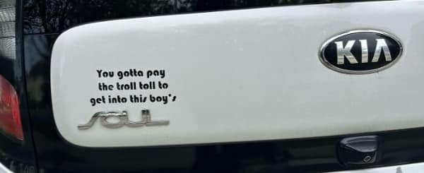 A funny bumper sticker on a silver car that reads I DON'T SUFFER FROM INSANITY - I ENJOY EVERY MINUTE OF IT in a bold, jagged yellow and white font on a black background.