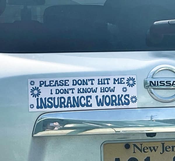 A funny bumper sticker on a light blue car that reads PLEASE DON'T HIT ME I DON'T KNOW HOW INSURANCE WORKS in blue bubble letters surrounded by simple white and blue daisy illustrations.