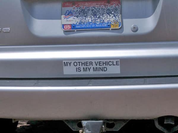 A [funny bumper sticker] parody on a red sedan's trunk lid that mocks the classic 'Baby on Board' signs. This yellow rectangular sticker features bold black text that reads: "BABY ON BOARD. (AND I'M LOSING MY MIND)."