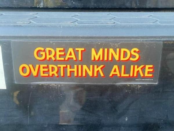A long rectangular [funny bumper sticker] on the rear gate of a black SUV centered below the window. It has red and white text apologizing for stress-induced parking rage: "I'M SORRY FOR WHAT I SAID WHEN WE WERE PARALLEL PARKING." It includes a cartoon illustration of a distressed driver.