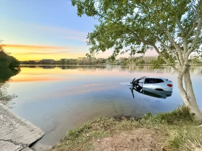 Large white utility truck tipped completely on its side across two parking spaces in suburban lot