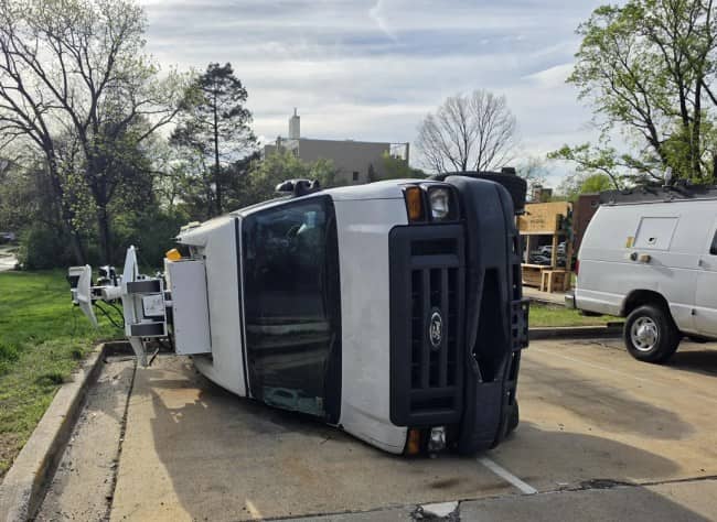 Large white utility truck tipped completely on its side across two parking spaces in suburban lot