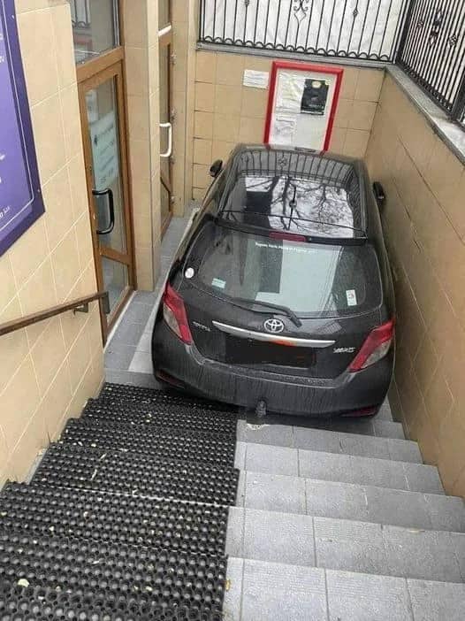 Black Toyota Yaris driven down indoor staircase and wedged against wall at bottom of building entrance steps