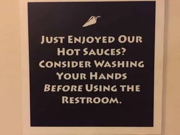 A restaurant sign suggesting customers wash their hands after eating hot sauce before using the restroom.