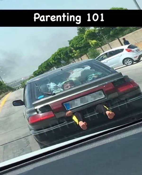 Car driving down a highway with a child's legs sticking out of the trunk area.