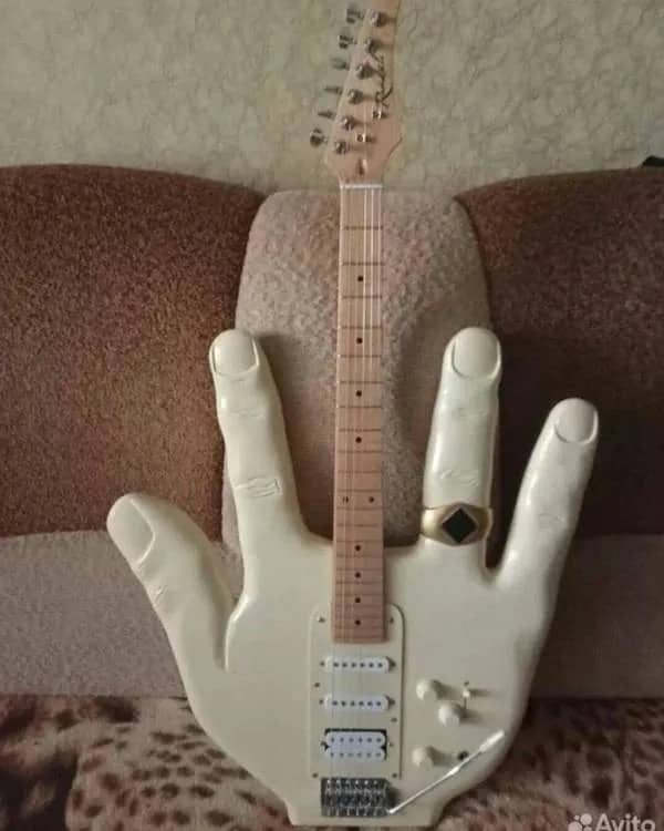 Custom white electric guitar with a body shaped like a large hand wearing a gold ring.