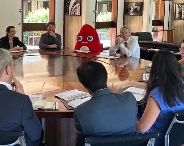 Surreal business meeting with a red mascot sitting at a large round table with professional executives.