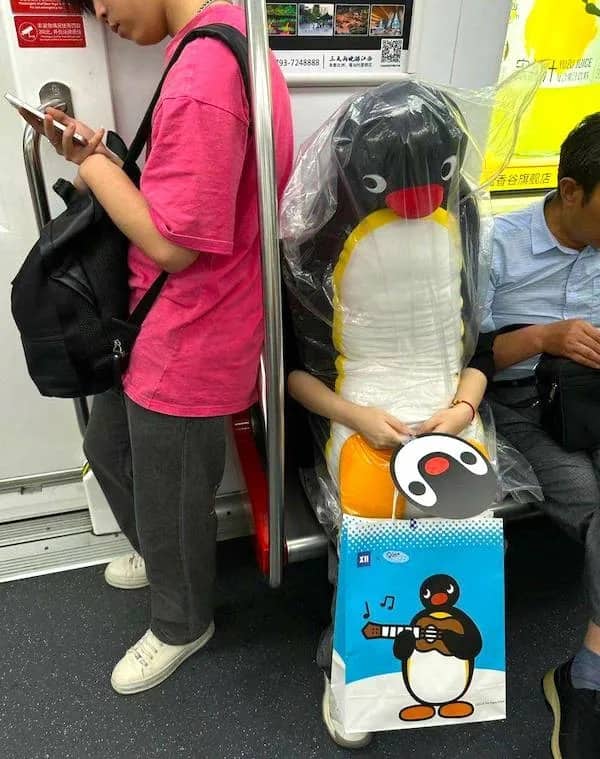 Candid photo of a person on a subway sitting with a giant, human-sized Pingu penguin plush.