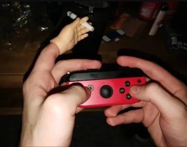 Gamer holding a red controller while wearing a tiny plastic hand on their finger holding a cigarette.