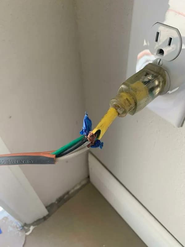 A "fire hazard 101" funny Osha violation picture of an electrical cord where the yellow jacket is torn open, revealing exposed copper wires crudely twisted together and "secured" with a single, tiny piece of blue electrical tape.