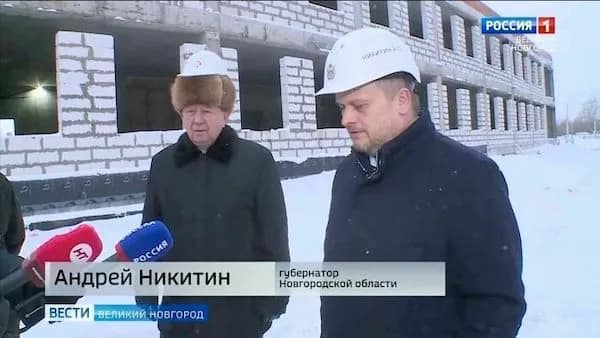 A funny osha violation picture from a snowy Russian construction site showing a man wearing a safety hard hat perched absurdly high on top of a thick fur ushanka hat.