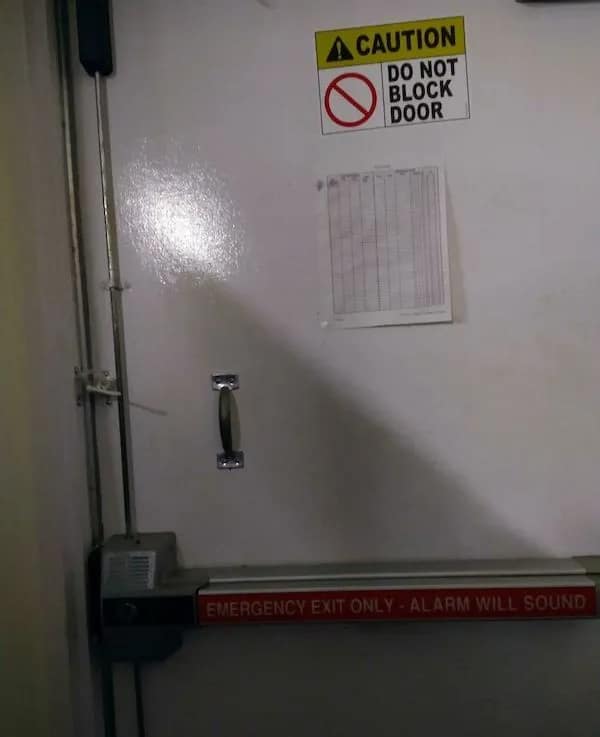 peak irony funny picture showing an emergency exit door with a "DO NOT BLOCK DOOR" sign that is currently being blocked by a security bar zip-tied across the frame.