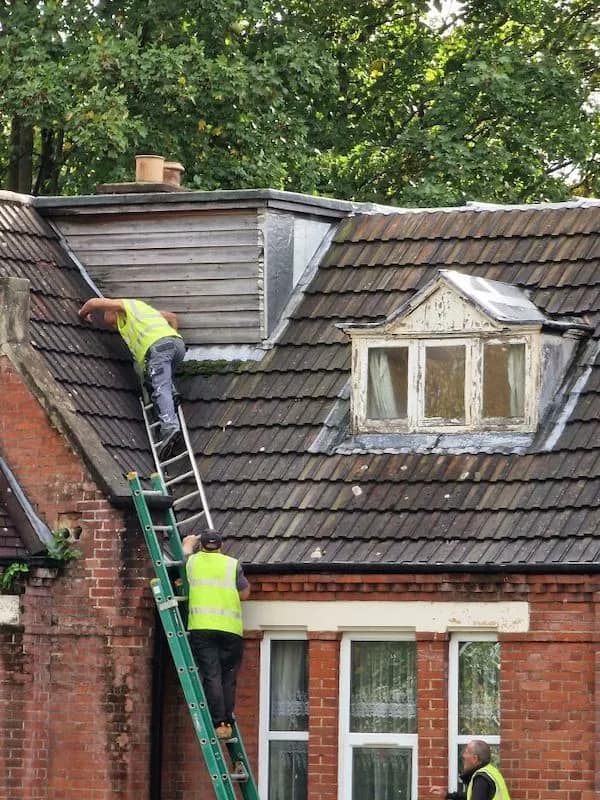double-stacked funny osha violation picture of roofing contractors using an extension ladder that is propped up on the top rungs of a second extension ladder below it to reach a high dormer, defying both gravity and common sense.
