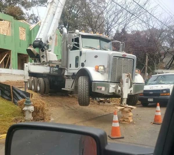 A gravity-defying funny Osha violation picture of a massive concrete pump truck with its front wheels dangling several feet in the air, supported only by a front outrigger resting on a shaky, leaning tower of thin wooden scrap blocks.