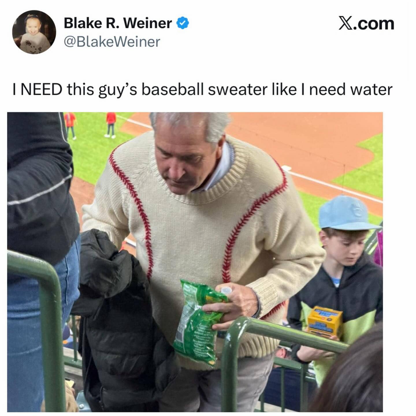 Man at a baseball stadium wearing a unique sweater designed to look like a giant baseball.