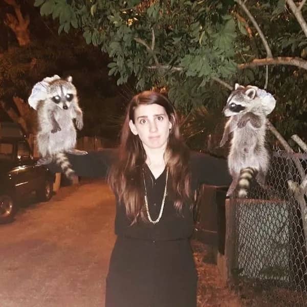Woman looking surprised while holding two raccoons in her arms outside at night in funny pics.