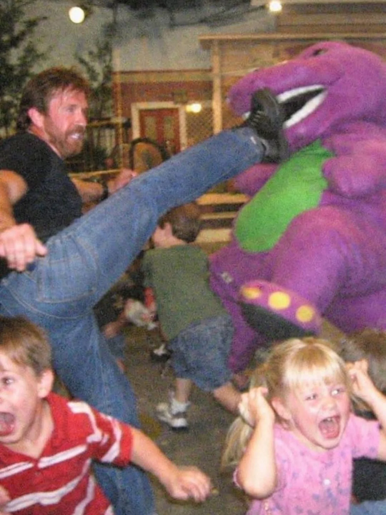 Action photo of Chuck Norris performing a high kick to the face of a purple dinosaur mascot.