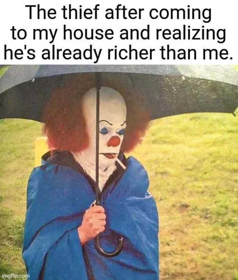 funny relatable meme featuring the 1990 version of Pennywise the Clown standing in the rain under an umbrella, looking dejected and smoking a cigarette. The text describes the awkward moment a thief breaks into your home only to realize they have a higher net worth than you do.
