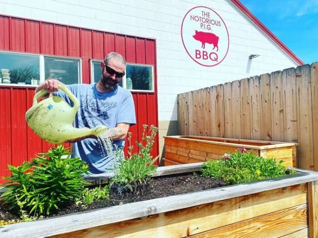 The Notorious P.I.G. BBQ restaurant exterior with man watering garden boxes, hip-hop themed name.