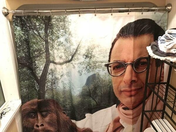 A cinematic funny shower curtain featuring a massive, close-up print of Jeff Goldblum’s face wearing stylish glasses and a scarf. He is set against a jungle background where a large gorilla peeks out from the foliage beside him.