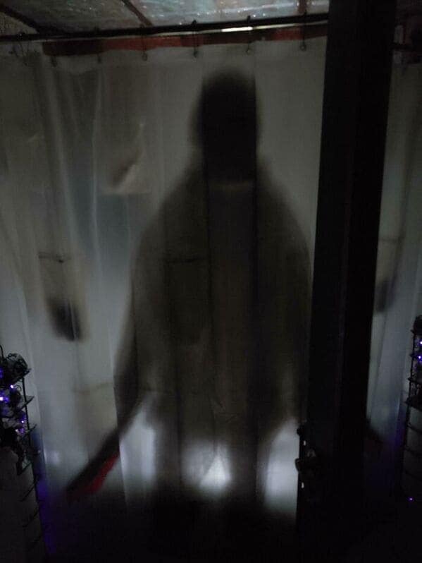 A terrifyingly funny shower curtain that uses light and shadow to create a silhouette effect. It shows a tall, slender, dark figure standing perfectly still behind the translucent white fabric, effectively giving every bathroom guest a heart attack upon entry.