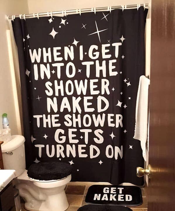 A text-based funny shower curtain in bold white lettering on a black starry background. The punchline reads: "WHEN I GET INTO THE SHOWER NAKED THE SHOWER GETS TURNED ON," paired with a matching "GET NAKED" floor mat for maximum commitment to the bit.