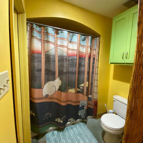 A sophisticated yet funny shower curtain styled after traditional Japanese Ukiyo-e art. It shows a white cat sitting on a wooden ledge, looking out through a shoji-style window at a distant Mount Fuji during a red sunset.