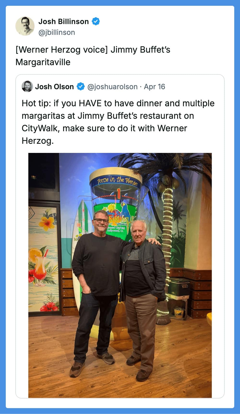 A funny tweet reply featuring a real photo of director Werner Herzog standing with a fan in front of a giant blender at Jimmy Buffett’s Margaritaville. The text simply reads, "[Werner Herzog voice] Jimmy Buffet’s Margaritaville," inviting a nihilistic internal monologue.