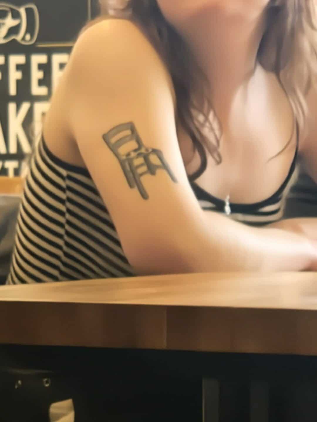 Woman with small chair tattoo on her upper arm creating an armchair visual pun
