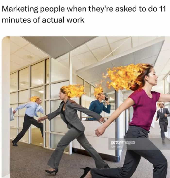 A hyperbolic funny work meme using a stock photo of corporate employees running through an office with their hair literally on fire. The text roasts the department's stamina, reading: "Marketing people when they're asked to do 11 minutes of actual work."
