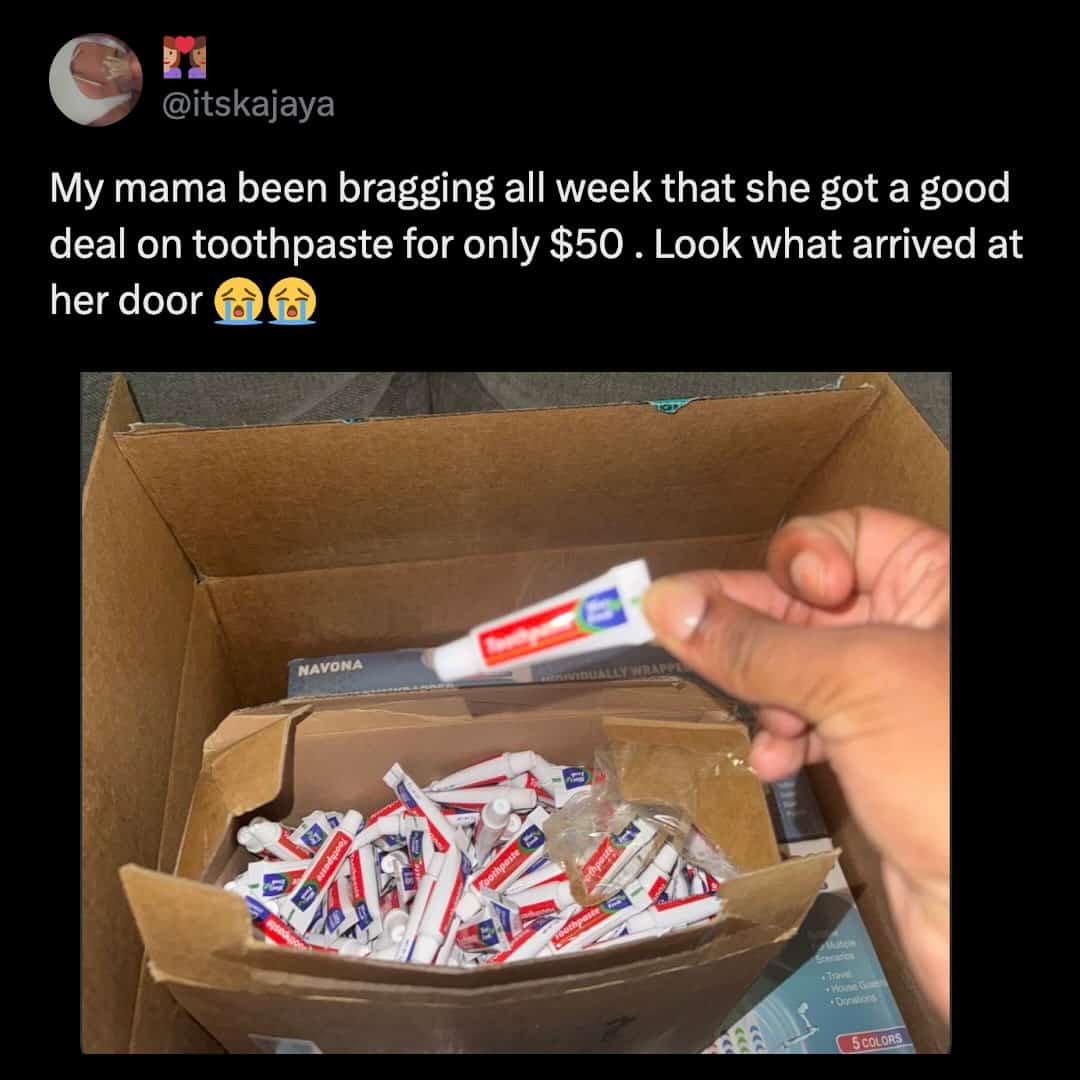 Hand holding a tiny sample-sized tube of toothpaste from a box of dozens.